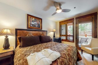 A hotel room with a king-sized bed, a white chair, a wooden headboard, and a ceiling fan.
