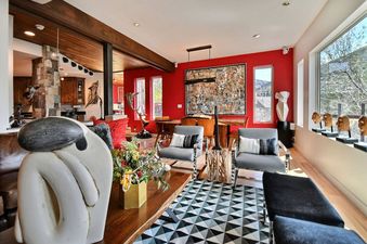 A vibrant living and dining area with red accent walls, modern furnishings, and large windows offering views of the outdoors.