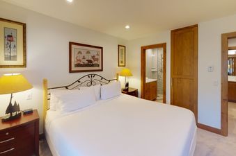 A bedroom with a king-sized bed, a bedside table with a lamp, and a door to the bathroom.