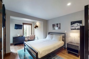 The bedroom in Fallridge 312 features a queen-sized bed, a dresser with a TV, a cozy chair, and large windows offering natural light.