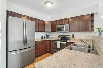 A modern kitchen with dark wood cabinets, light countertops, and stainless steel appliances.