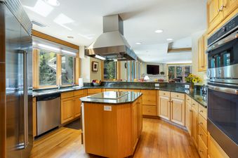 Modern kitchen with wood cabinets, stainless steel appliances, a central island, and views of pine trees.