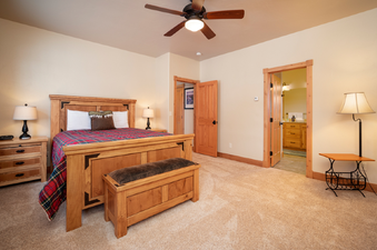 A rustic bedroom with a wooden bed frame, plaid bedding, and a ceiling fan.