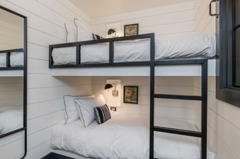 A bunk bed with white bedding is in a small bedroom with white walls and a mirror