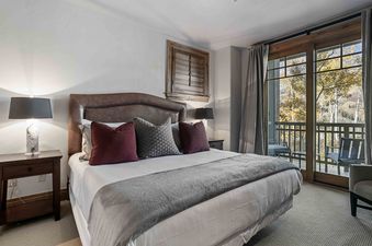 The master bedroom features a cozy bed with a leather headboard, decorative pillows, and bedside lamps, overlooking an autumn mountain view from the balcony.