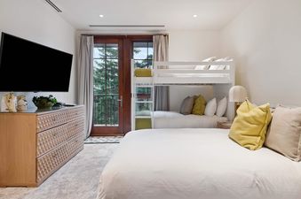 The bedroom features a light wood dresser with a television mounted above it, a comfortable queen-size bed, and a bunk bed, creating a versatile and inviting space.