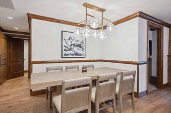 The dining room in The Aspen 30B, with a wood table and chairs. There is a light fixture above the table, and a painting on the wall.