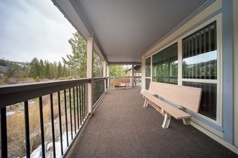 A long, covered porch with benches and a railing offers a view of a forested valley.