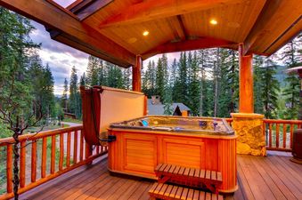 The Alders Chalet features a private hot tub on a wooden deck, surrounded by lush green trees under a vibrant sky.