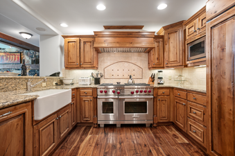 The kitchen in Grand Lodge Three Bedroom Deluxe 404 features dark wood cabinets, a large farmhouse sink, granite countertops, stainless steel appliances, a double oven, and a gas cooktop.