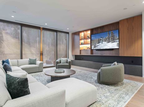 A modern and spacious lounge area in Founders Place 2503 featuring a sectional sofa, armchairs, and a large media wall.