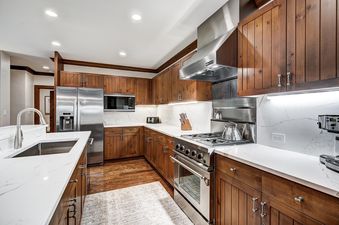 The kitchen at Snow Cloud Lodge 515 showcases dark wood cabinetry, white marble countertops, and modern stainless steel appliances including a refrigerator, microwave, and gas range.