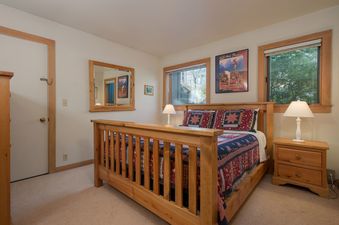 A rustic bedroom in Rendezvous A2 with a wooden queen-size bed, colorful quilt, wooden nightstands with lamps, and large windows.