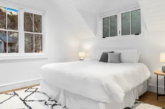 Bright white bedroom at Top Camp with king bed and mountain views through windows.