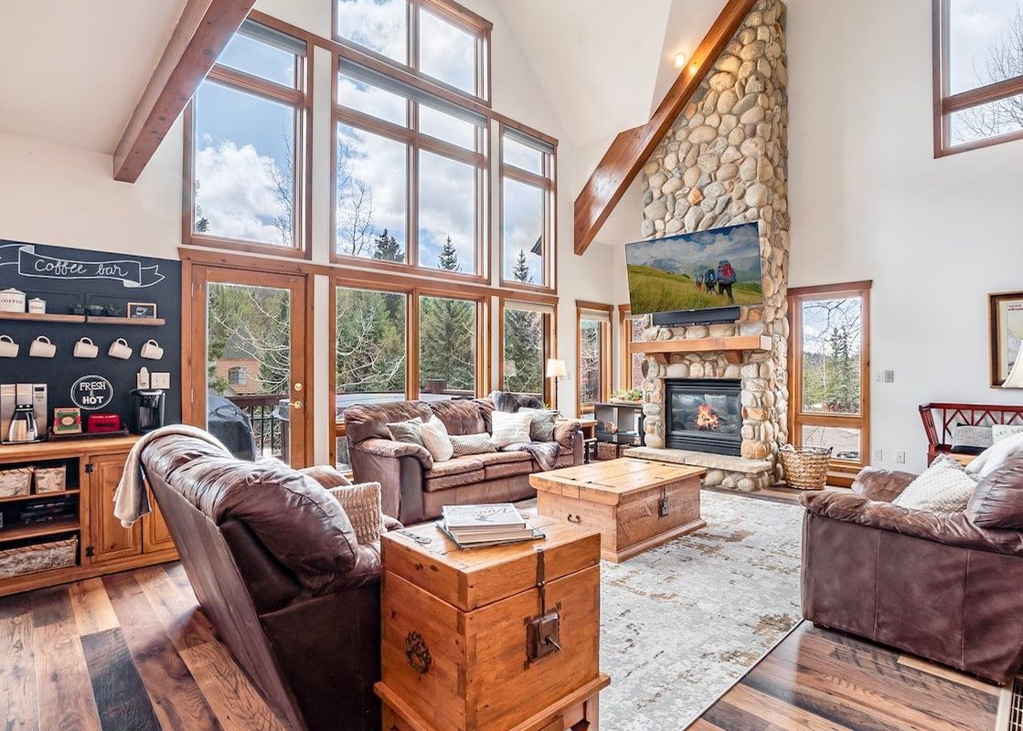 A cozy, sunlit living room at Trademark Views featuring a stone fireplace, large windows, and comfortable leather seating.