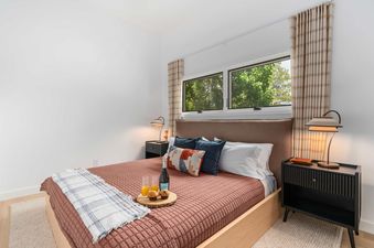A cozy bedroom with a queen bed, wooden nightstands, and a window displaying green trees at Cottonwood Jackson Hole.