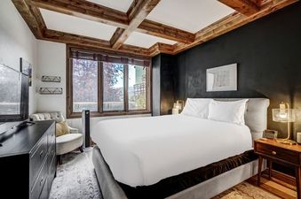 A cozy bedroom in Arrowhead Village Condominium Premium 1 Bedroom featuring a plush bed, rustic wooden beams, and a window with a view of the surrounding landscape.