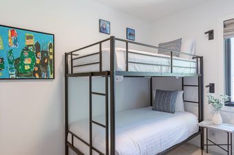A brightly lit children's bunk room at Whiteridge B7, featuring a modern metal bunk bed with white bedding, colorful artwork, and a window with a Roman blind.