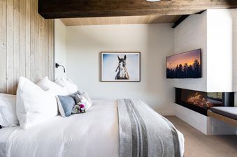 The bedroom at Moonlight Basin 6A Treeline Springs features a king-size bed with white linens, fluffy pillows, and a gray striped throw blanket. There is a fireplace with a modern design, and a large flat-screen TV mounted to the wall. The decor is simpl