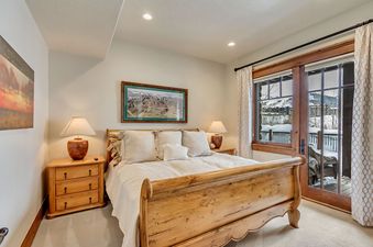 Cozy master bedroom in The Lookout Home featuring a wooden sleigh bed and glass doors opening to a snowy mountain view.