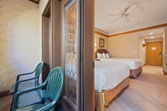 A bright bedroom in The Charter G215 with two beds and an adjacent balcony access with two green chairs.
