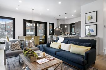 A modern open-concept living room, dining area, and kitchen are visible in Juniper 901, featuring a navy sofa, patterned armchairs, a wooden coffee table, and a contemporary kitchen with gray cabinets and stainless steel appliances.