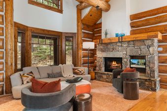 A rustic living area with a stone fireplace, log walls, and cozy modern seating in Timber Ridge at Jackson Hole.