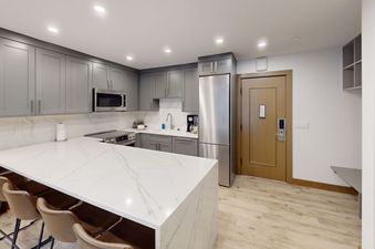 A modern kitchen with a breakfast bar, stainless steel appliances, and light wood floors.