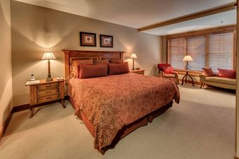 A bedroom with a king-sized bed, two nightstands with lamps, a dresser, and a window with blinds.