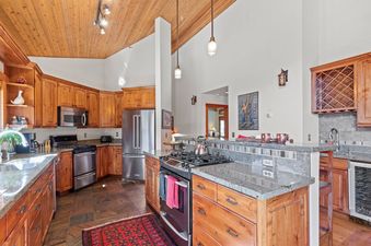 The gourmet kitchen at Crescent Cabin features warm wooden cabinetry, granite countertops, and stainless steel appliances under a vaulted wooden ceiling.