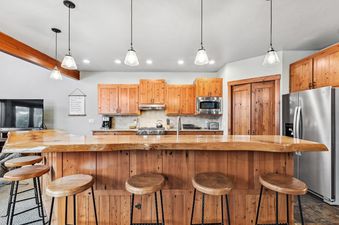 A rustic kitchen at Chair View Chalet featuring wooden cabinetry, stainless steel appliances, a live-edge wooden bar with four stools, and pendant lighting.