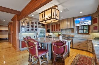 The gourmet kitchen at Timber Lodge at the Oaks features a rustic yet luxurious design with a large central island, antler bar stools, modern appliances, and a nature-inspired chandelier.