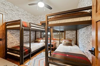 The bunk room at Central Loft 303 features two dark wooden bunk beds with white bedding, brown and red striped blankets, and whimsical owl-patterned wallpaper.