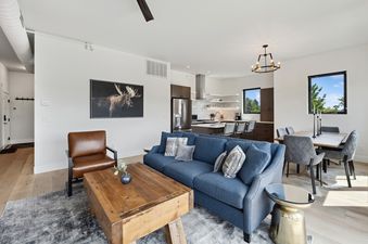 An expansive open-concept living space at ViewTopia, featuring a blue sofa, wooden coffee table, dining area, and a modern kitchen with natural light.