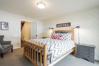 A bedroom with a queen-sized bed, a wood frame, and a white chevron duvet, bedside table, and an armchair in the corner.