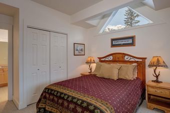 The bedroom of Moonlight Basin Saddle Ridge B5 features a king bed with a burgundy and gold patterned comforter, two side tables, and a large window with a view of the mountains.