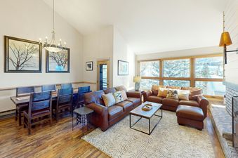 Living room in Kutuk 310 with leather sofas, a coffee table, a rug, a fireplace, and large windows with views of the trees and snow.