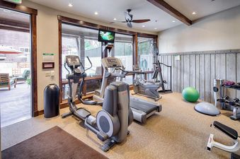 The Silver Star 1104 gym features modern exercise equipment including treadmills, ellipticals, and weights, set within a bright room with large windows overlooking an outdoor patio.