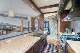 The kitchen in See Forever San Sophia 114 3BR 4BA features granite countertops, a double sink, a gas range, wooden cabinetry, and pendant lighting, with large windows overlooking a snowy mountain landscape.