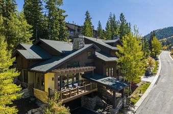 The Deer Valley Lookout 26 is nestled among vibrant green and yellow trees on a clear, sunny day, with a winding road leading past it.