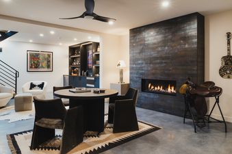 A stylish living area at Oatgrass Escape featuring a dark tiled fireplace, a round dining table, a bar, and unique decor with warm lighting.