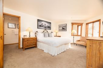 A master bedroom at Snow Park Chalet featuring a king-sized bed, two nightstands with lamps, a large framed artwork of a bear, a mirror, and a leather armchair.