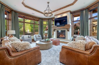 Cozy living room at The Pinnacle at Powder Ridge with leather sofas, stone fireplace, and large windows looking out to the green ski hills.