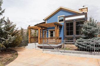 A blue villa with a wooden pergola and a concrete pathway surrounded by green trees.