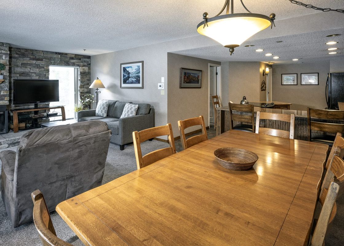 A spacious open-concept living and dining area at The Corporate Suite Beaver Run Resort, featuring a large wooden dining table, a cozy gray sofa, a fireplace, and a flat-screen TV.