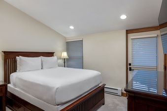The comfortable bedroom in Landmark 210 features a dark wood bed with white bedding, soft carpet, and warm lighting, creating a serene and inviting space.
