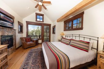 A luxurious bedroom at Fox Paw Lodge features a king-sized bed with colorful bedding, a stone fireplace, and a private balcony.