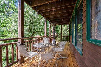 A private balcony at Cottonwood 204 with an outdoor dining set and patio heater, surrounded by lush trees and featuring wooden floors and green-framed windows.