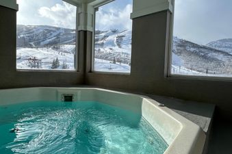 A hot tub with sparkling turquoise water offers a panoramic view of snow-covered ski slopes and mountains through large windows.