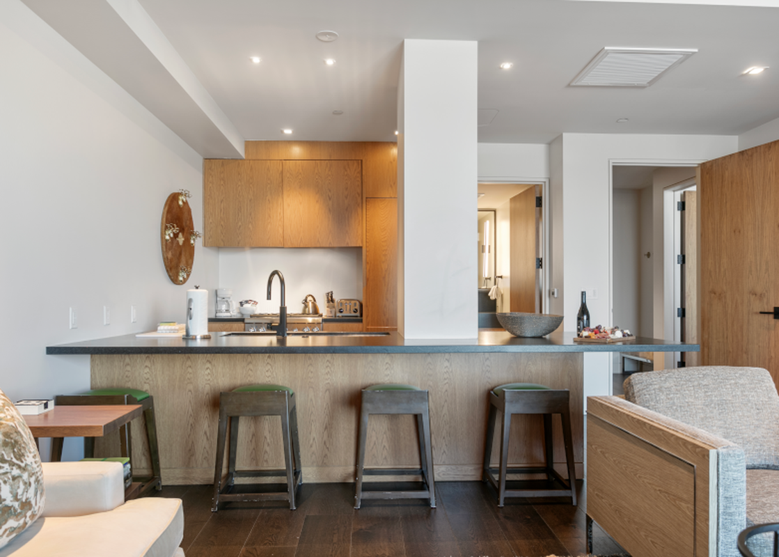 A modern kitchen with a breakfast bar, stools and a couch in the living room.